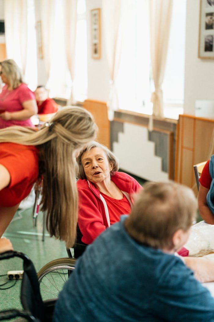 Elderly woman in a wheelchair engaging with caregiver in a bright, welcoming environment.
